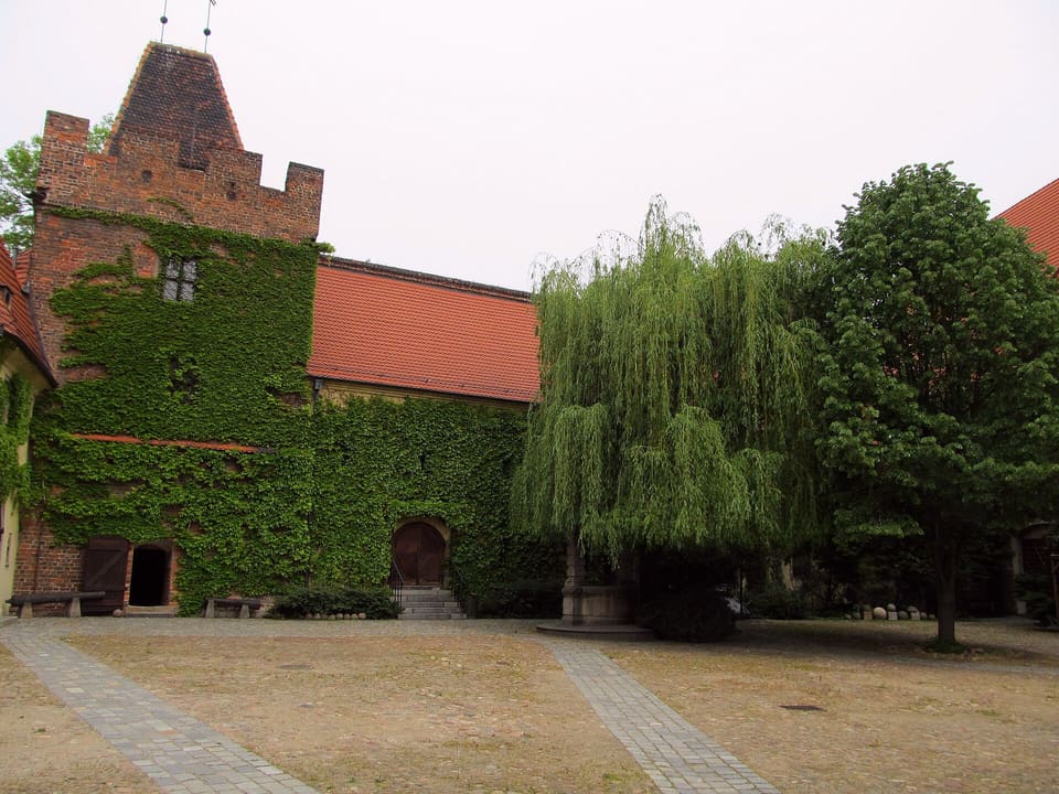 The Arsenal's inner courtyard: an ivy-covered corner tower and red-tiled roofs, with a willow beside a stone well.