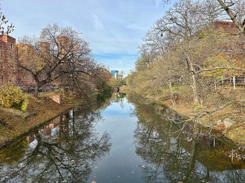 The City Moat in autumn, a calm straight canal between grassy banks and bare trees, seen from the Kładka Sądowa.