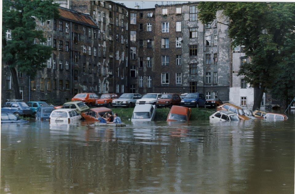 A flooded courtyard between tenement blocks in July 1997, parked cars submerged to their roofs in brown water.