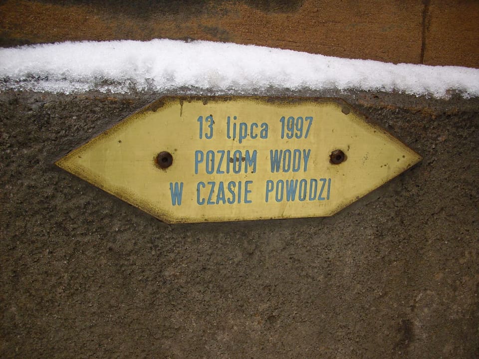A small brass plate fixed to a wall, lettered “13 lipca 1997 — poziom wody w czasie powodzi”, marking how high the water stood.