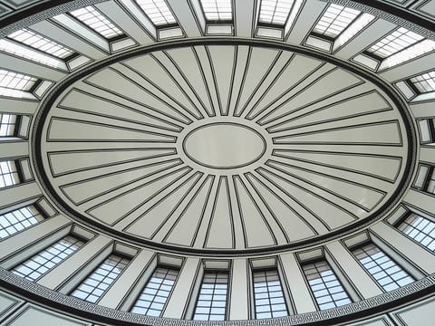 Blick nach oben in eine der Kuppeln: eine ovale Decke mit Rippen, die von einem mittleren Oval ausstrahlen, umgeben von verglasten Fenstern.