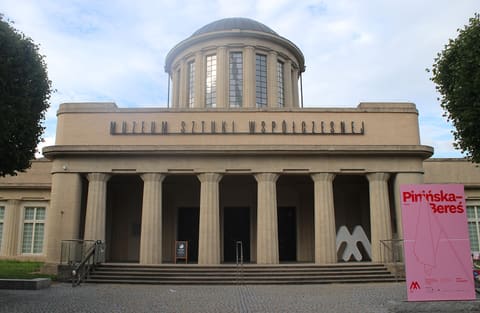 Die Eingangsfront des Pavillons: eine Reihe hoher Säulen unter dem Schriftzug des Museums für zeitgenössische Kunst, dahinter eine Kuppel.