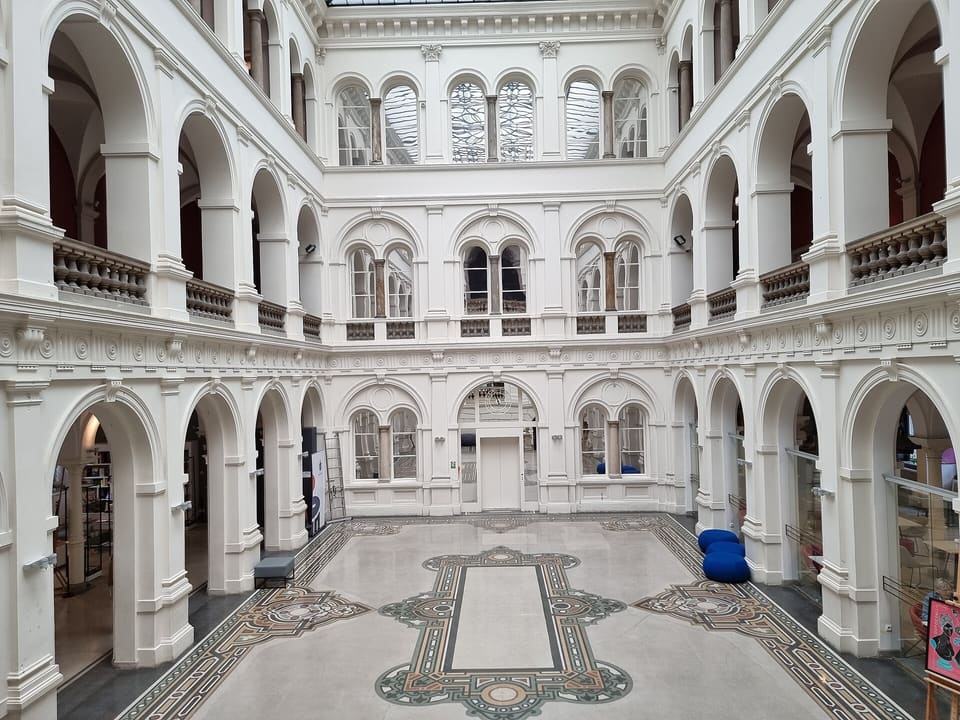 Der glasüberdachte Innenhof des Museums mit drei Geschossen weißer Arkaden rund um einen gemusterten Steinboden.