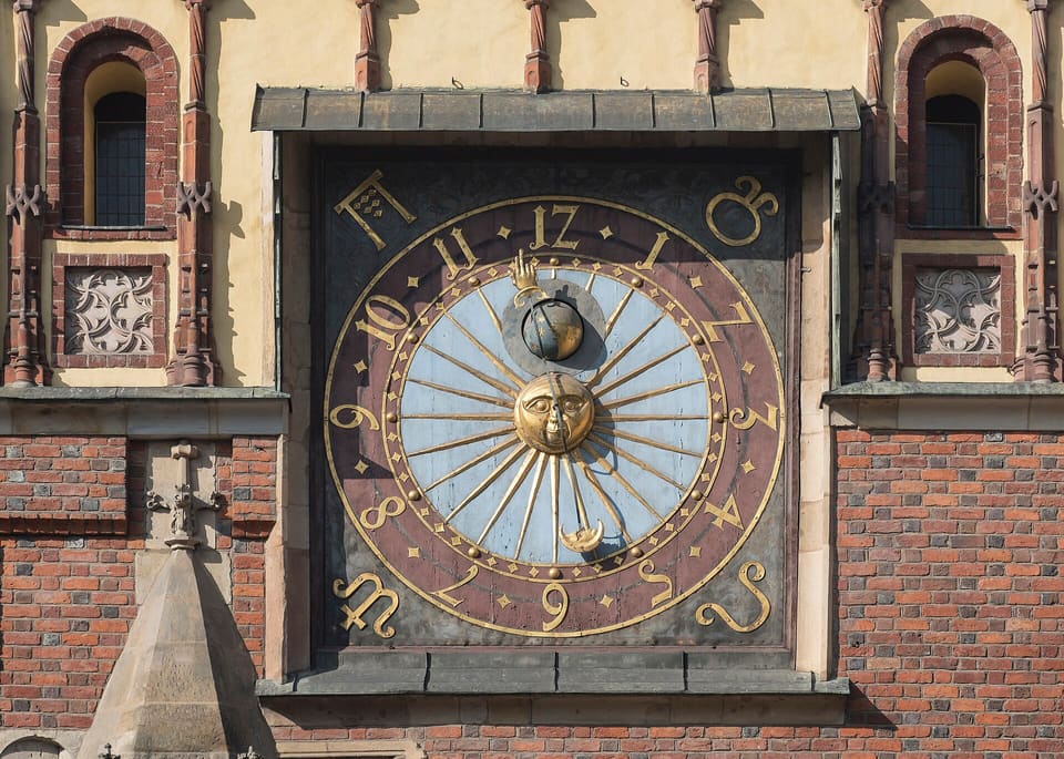 A close view of the astronomical clock on the Old Town Hall's east gable, with its gilded dials, flanked by two traceried windows.