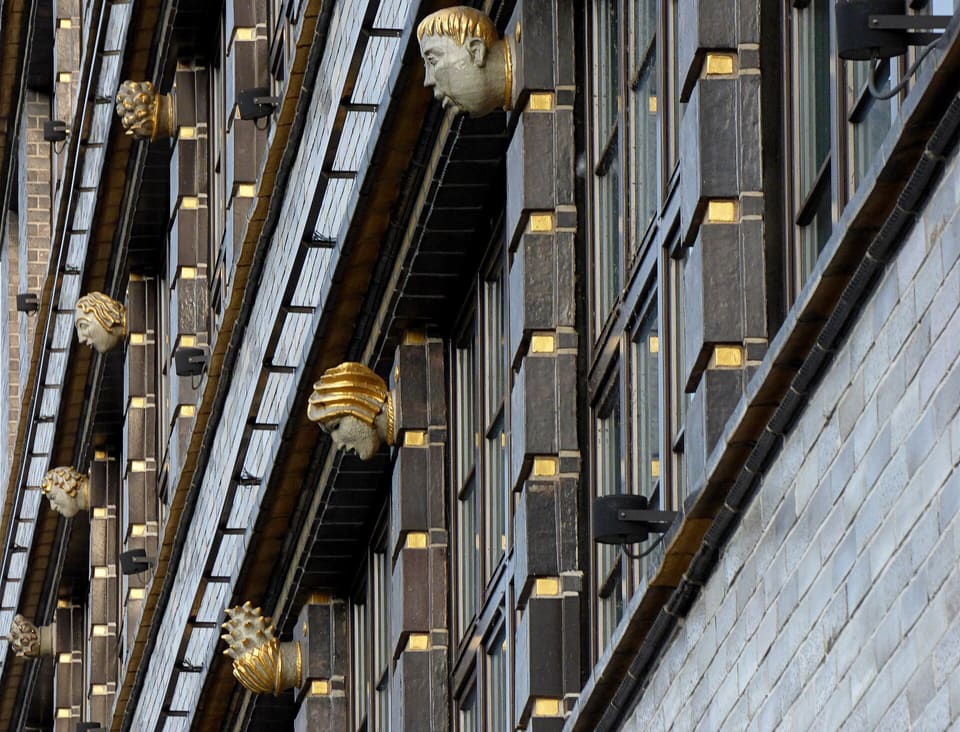 Nahansicht der Keramikverkleidung der Fassade mit vergoldeten skulptierten Köpfen in den dunklen Pilastern zwischen den Fensterreihen.