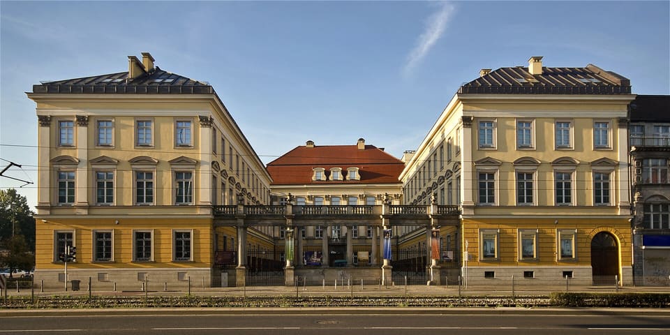 The street front of the Royal Palace: two long cream and yellow wings facing each other, with a lower red-roofed block between them behind a balustraded colonnade.