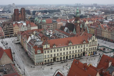 A view down onto the Market Square from a church tower, showing the Old Town Hall's tower and gabled roofline, rows of houses lining the square, and brick church towers in the distance.