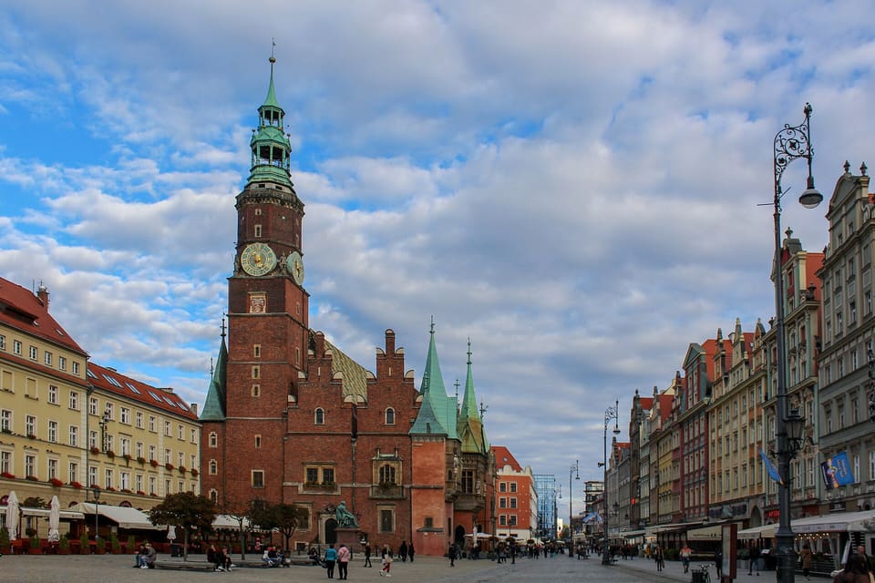 The brick Old Town Hall with its clock tower stands in the Market Square, with tenement houses on both sides under a blue sky with clouds.