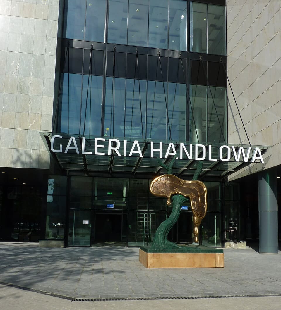 «Профіль часу» Далі перед входом у Sky Tower, під вивіскою Galeria Handlowa: бронзовий годинник, що розтікається, перекинутий через дерево, на низькому постаменті.