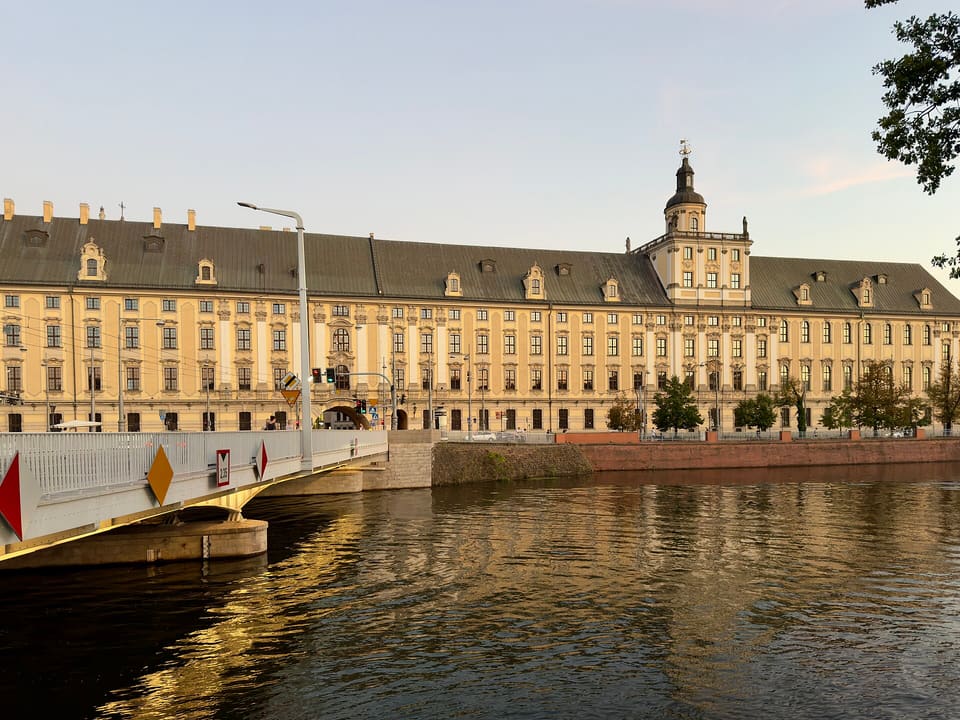 Die lange gelbe Fassade des Hauptgebäudes der Universität an der Oder, mit dem Mathematischen Turm in der Mitte, von der Brücke aus gesehen.